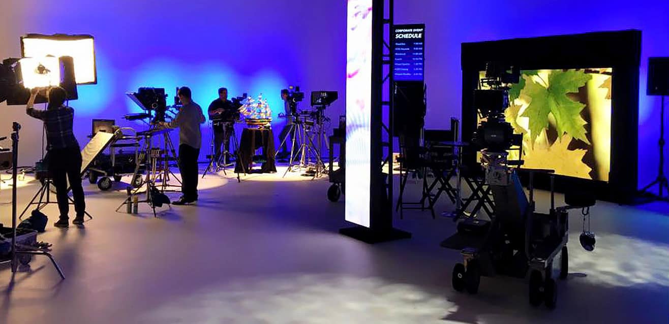 Production studio with cameras, lighting equipment, and digital screens set up, showcasing a professional video production environment.