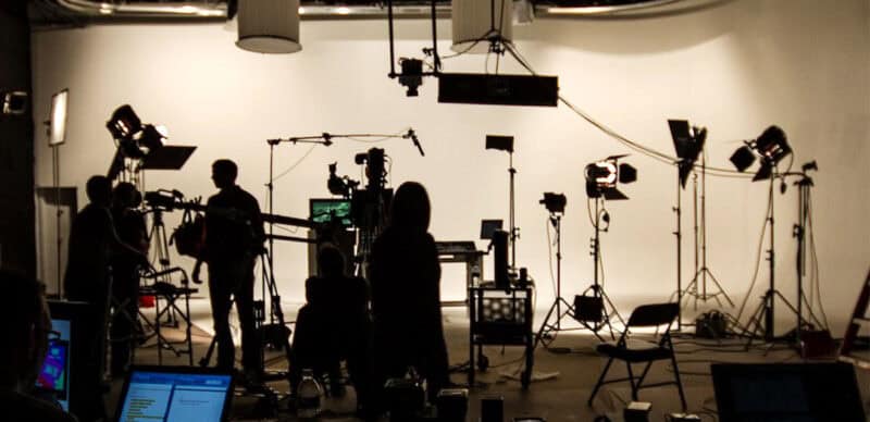 Video production studio with crew, lighting equipment, and cameras set up for filming on a white cyclorama background.