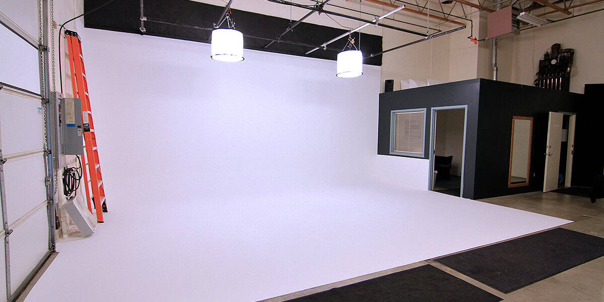 Empty view of our Stage B at Pixthis Stage Rentals and Productions in Portland, featuring a white cyclorama wall, overhead lighting, a roll-up door, and a production office, showcasing affordable video production studio rental costs with video editing services in Portland. 