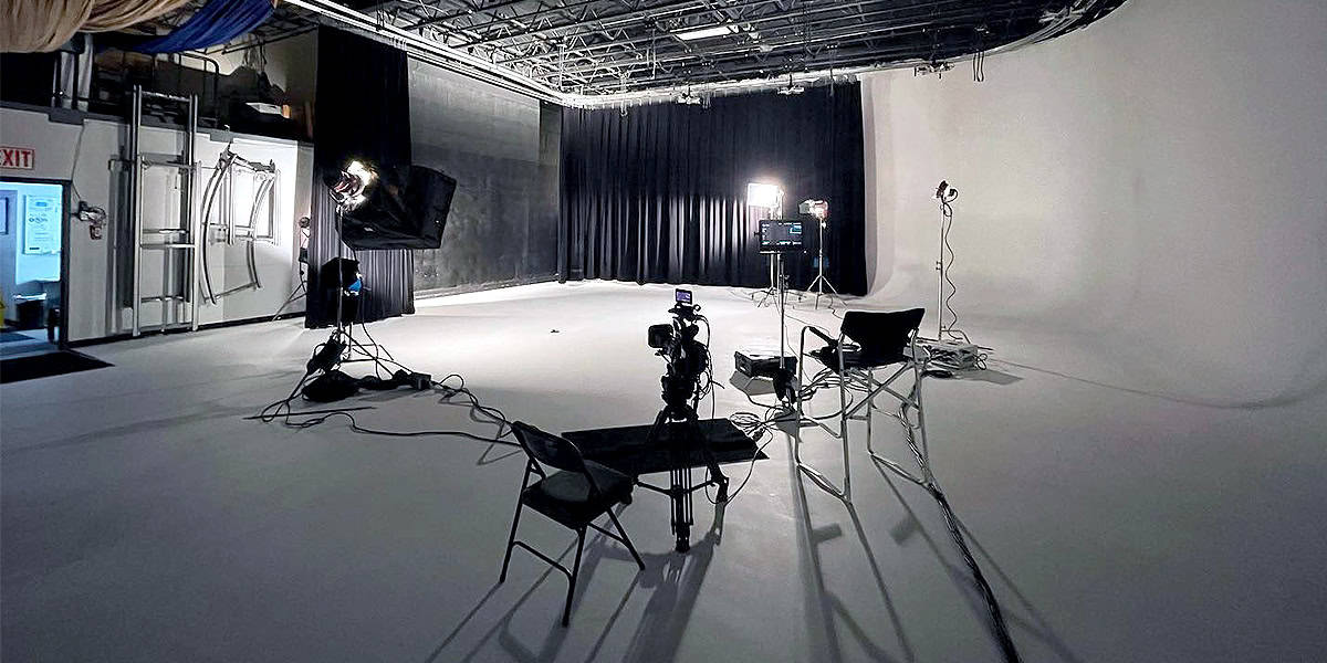 Professional video production studio setup with cameras, lighting equipment, and chairs arranged on a white cyclorama background, showcasing an ideal environment for filming projects such as broadcast productions, feature films, or corporate content using high-performance cameras like the Sony PDW-F800