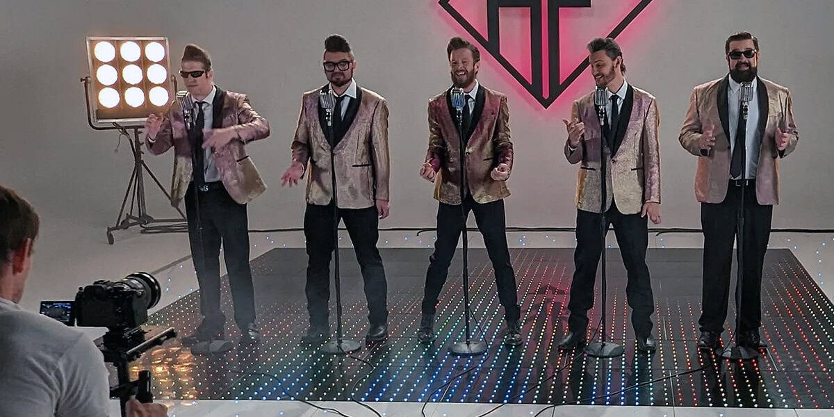Band in shiny jackets performing on a professional sound stage at Pixthis in Portland, filmed with a camera and lighting setup, featuring a colorful LED floor and neon backdrop for a music video shoot.