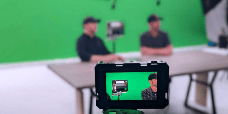 Close-up of a camera monitor in a green screen studio at Pixthis in Portland, showing a filming setup with two people at a table, capturing a professional video production with chroma key background.