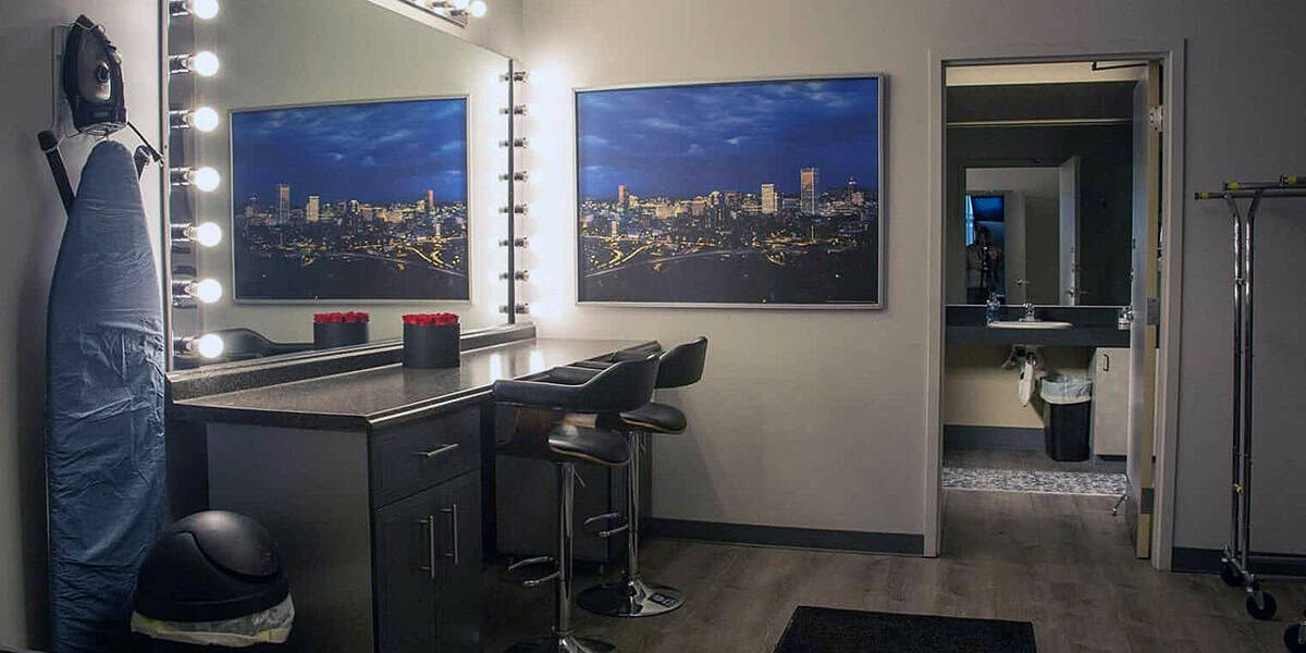 Makeup and wardrobe area at Pixthis in Portland, featuring a vanity with Hollywood-style lighting, two stools, an ironing board, and cityscape artwork, providing a comfortable space for crew preparation.