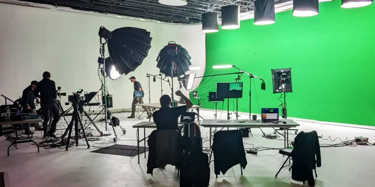 Production team working on a green screen studio set with lighting and cameras