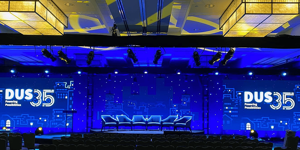 Professional event AV setup with colorful LED uplighting, large projection screens, and Shure audio system at a Portland conference by Pixthis
